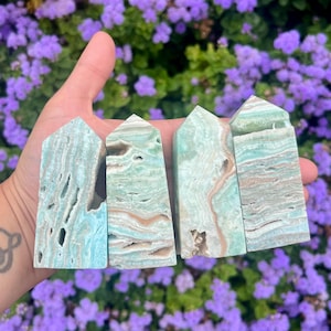 May include: Four green and brown banded, polished,  faceted,  crystal towers. The towers are arranged in a row from left to right, with the tallest tower on the left and the shortest tower on the right.