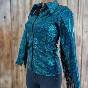 Puede incluir: Una camisa azul turquesa con flecos negros en las mangas. La camisa tiene una cremallera y un cuello.
