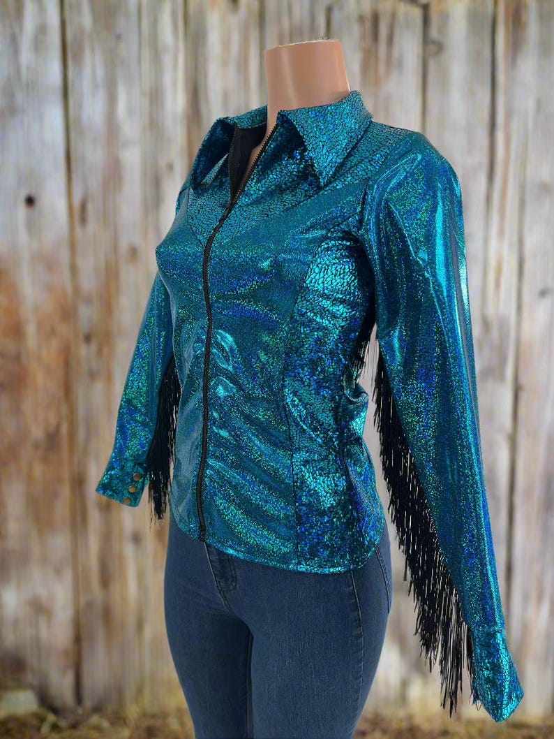 Puede incluir: Una camisa azul turquesa con flecos negros en las mangas. La camisa tiene una cremallera y un cuello.
