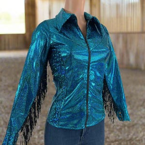 Puede incluir: Una camisa vaquera azul turquesa brillante con flecos negros en las mangas y cierre de cremallera.