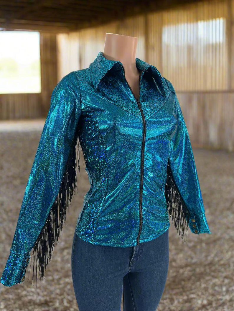 Puede incluir: Una camisa vaquera azul turquesa brillante con flecos negros en las mangas y cierre de cremallera.