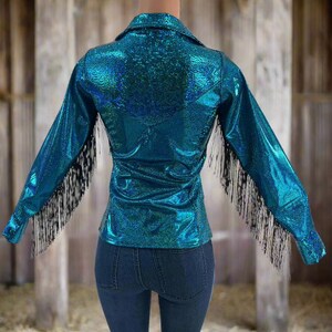 Puede incluir: Una camisa azul turquesa con ribetes de flecos negros. La camisa tiene un acabado brillante e iridiscente.