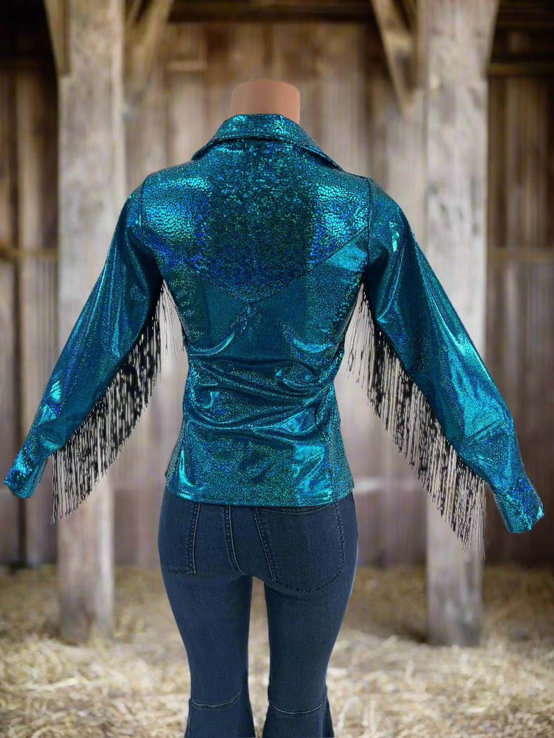 Puede incluir: Una camisa azul turquesa con ribetes de flecos negros. La camisa tiene un acabado brillante e iridiscente.