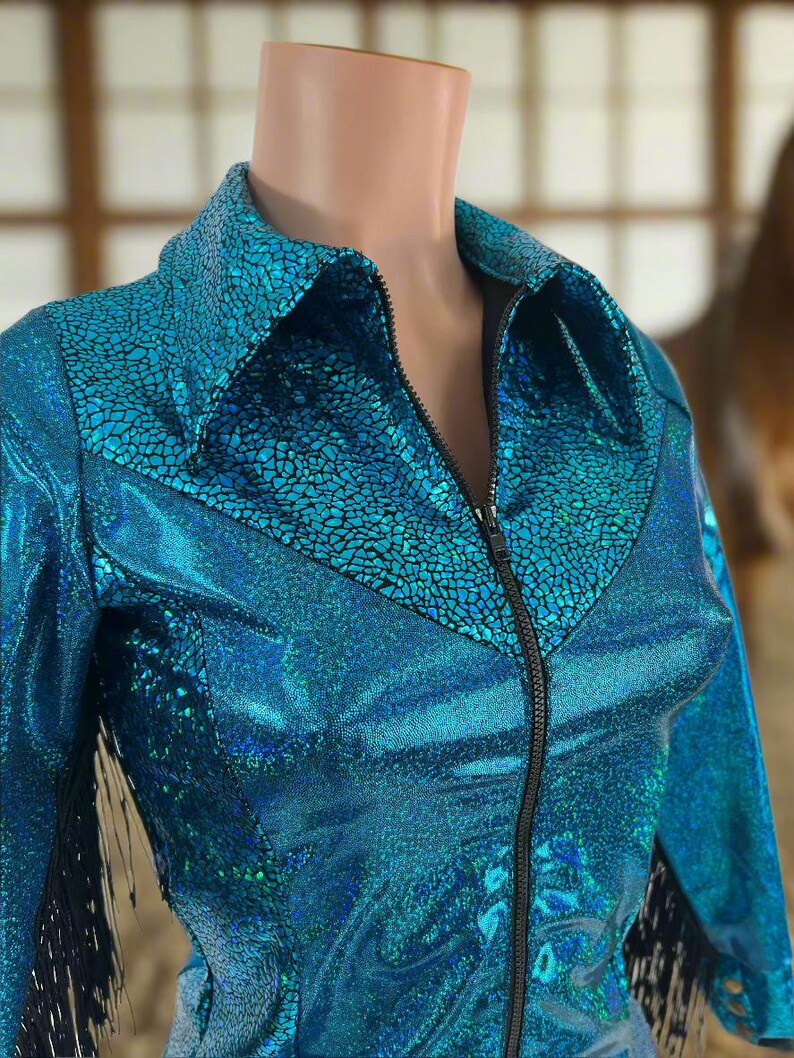 Puede incluir: Una chaqueta azul turquesa con cremallera negra y flecos negros. La chaqueta tiene un acabado brillante e iridiscente.