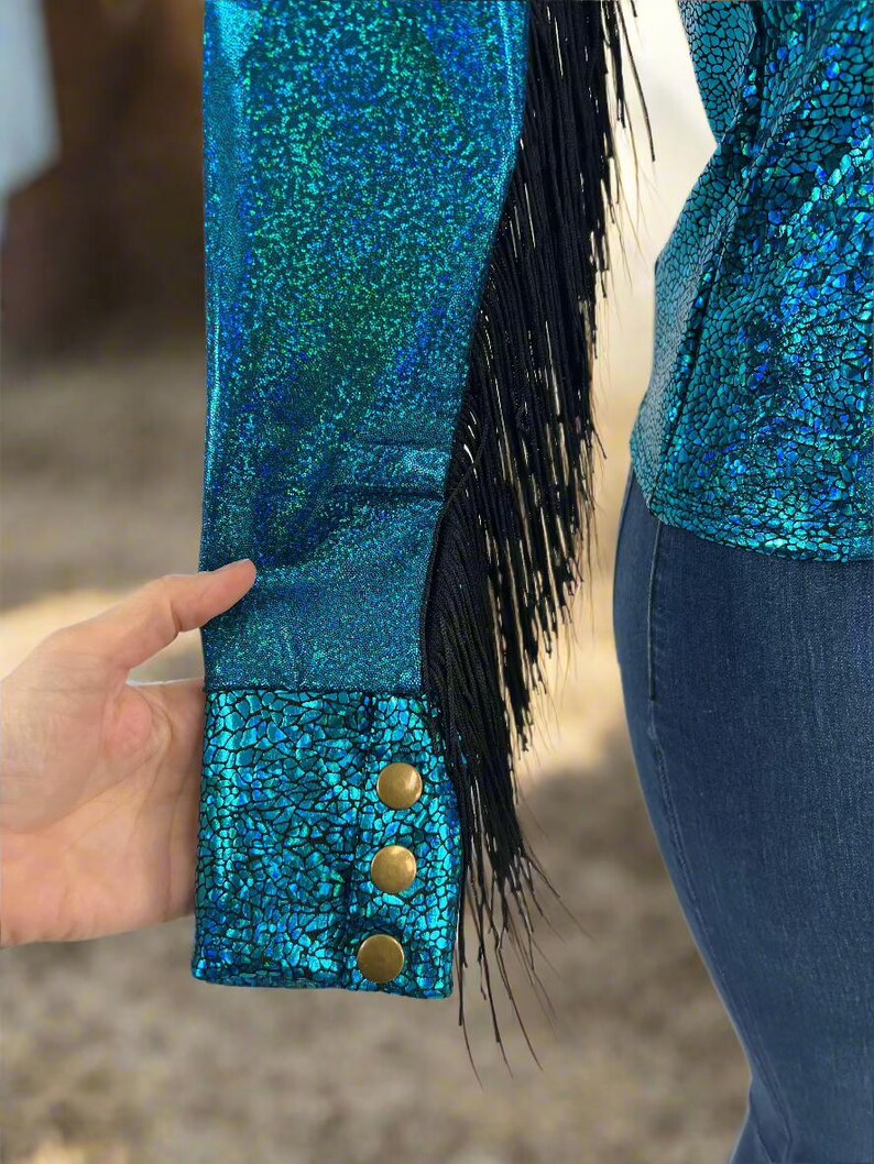 Puede incluir: Una camisa azul turquesa con ribetes de flecos negros y botones dorados en los pu&ntilde;os. La camisa tiene un acabado brillante e iridiscente.