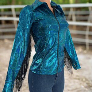 Puede incluir: Una camisa azul turquesa con flecos negros en las mangas y cierre de cremallera. La camisa est&aacute; hecha de una tela brillante e iridiscente.