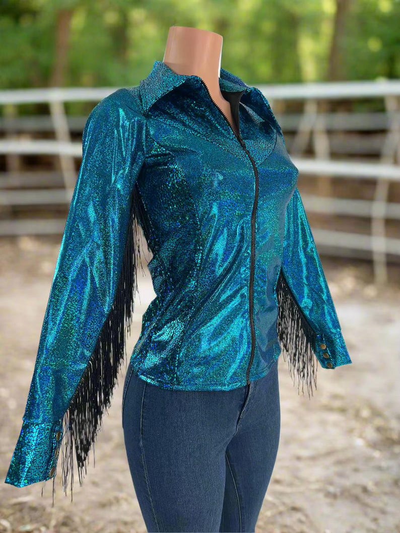 Puede incluir: Una camisa azul turquesa con flecos negros en las mangas y cierre de cremallera. La camisa est&aacute; hecha de una tela brillante e iridiscente.