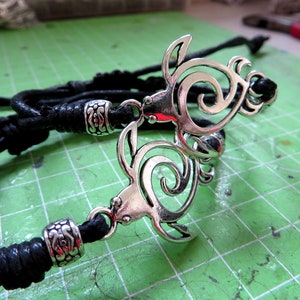 May include: A black leather cord necklace with a silver pendant featuring two intertwined turtle designs.