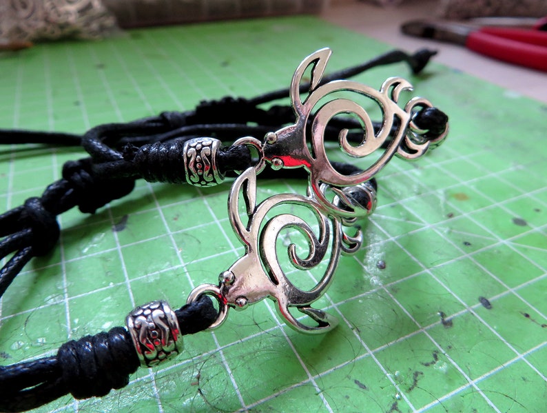 May include: A black leather cord necklace with a silver pendant featuring two intertwined turtle designs.