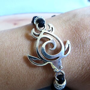 May include: A black cord bracelet with a silver turtle charm. The turtle is a stylized design with a swirl in the center.