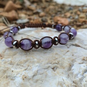 May include: A brown leather cord bracelet with amethyst beads and silver accents.