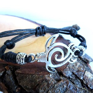 May include: A black cord bracelet with a silver turtle charm. The turtle is a cutout design with a swirl pattern.