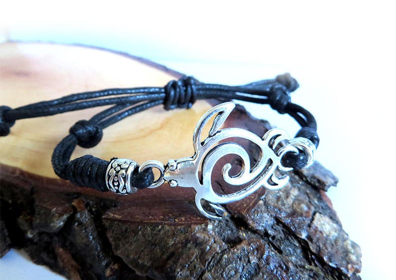 May include: A black cord bracelet with a silver turtle charm. The turtle is a cutout design with a swirl pattern.