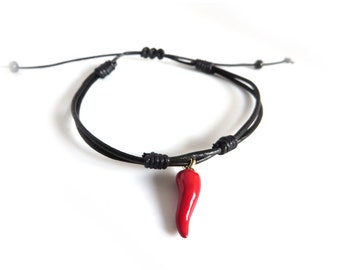 May include: A black leather bracelet with a red chili pepper charm. The bracelet is adjustable and has a simple design.