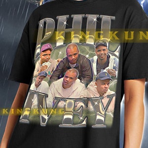 Pode incluir: Camiseta unisex preta com uma estampa gráfica de um grupo de homens usando chapéus e segurando cartas. O texto "KING" e "KUNG" está impresso na camiseta. A modelo está usando o tamanho XL.