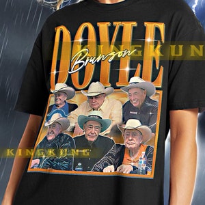 Pode incluir: Camiseta preta com um gráfico em estilo vintage com o nome "DOYLE" e "Bronson" em letras douradas. O gráfico inclui imagens de homens com chapéus de cowboy. A camiseta é um estilo unissex.