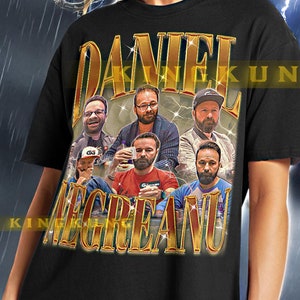 Pode incluir: Camiseta preta com um gráfico dourado de um grupo de homens com o texto "DANIEL NEGREANU". A modelo está usando uma camiseta tamanho XL.