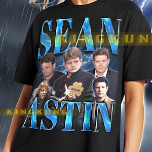 May include: Black unisex t-shirt with a graphic print of Sean Astin and the text "Sean Astin" in blue and white. The graphic features a collage of images of Sean Astin from different movies. The shirt is being modeled by a person wearing black leggings.