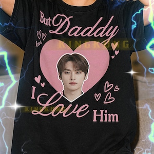 May include: Black t-shirt with the text "But Daddy I Love Him" in pink, featuring a heart-shaped graphic with a person's image. The shirt includes small heart graphics.