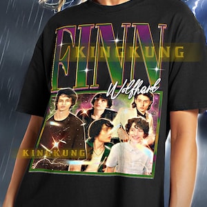 May include: Black t-shirt featuring a graphic of Finn Wolfhard and the text "FINN WOLFHARD" in a retro style. The shirt has a vintage aesthetic with a photo of the actor. The shirt is unisex.