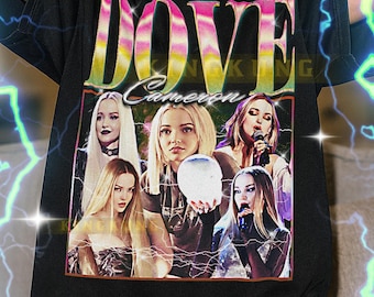 May include: Black unisex t-shirt featuring a graphic of Dove Cameron with the text "DOVE" in a colorful design. The shirt has a crew neck and short sleeves. The image includes the text "Cameron".