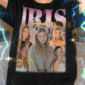 Może przedstawiać: Czarny t-shirt unisex z napisem "IRIS" w kolorze różowym i kolażem zdjęć pięciu kobiet. Koszulka ma okrągły dekolt i krótkie rękawy. Tekst "Kendall" znajduje się pod słowem "IRIS".