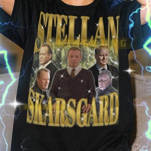 May include: Black t-shirt featuring the text "STELLAN SKARSGARD" in gold lettering, with a collage of portraits. The model is wearing an XL shirt. The shirt is unisex and fits true to size.