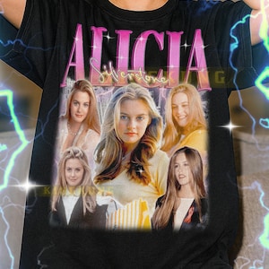 May include: Black t-shirt featuring the name "ALICIA Silverstone" in pink and white, with a collage of photos of the actress. The shirt is a unisex style.