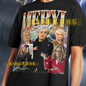 May include: Black t-shirt with a graphic print of four women from the movie "The Devil Wears Prada". The text "Meryl Streep" is printed in gold letters on the shirt. The shirt is a unisex style and fits true to size.