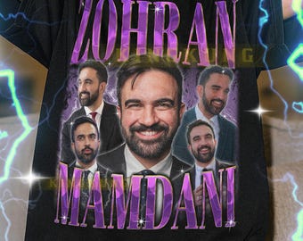 Può includere: T-shirt nero con grafica di un uomo sorridente e la scritta "ZOHRAN MANDANI" in viola. La maglietta ha girocollo e maniche corte. Il testo in fondo alla maglietta non è incluso.