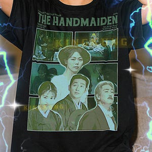 Puede incluir: Camiseta negra con un gráfico de la película "The Handmaiden". El diseño incluye el título de la película e imágenes de los actores. La camiseta la lleva una persona.
