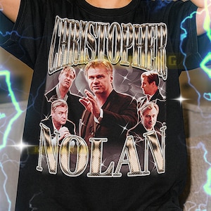 Könnte beinhalten: Schwarzes T-Shirt mit einer Grafik von Christopher Nolans Namen und Bild. Das Design enthält den Namen "CHRISTOPHER" über "NOLAN" in einem Vintage-Stil. Das Shirt ist ein Unisex-Stil.