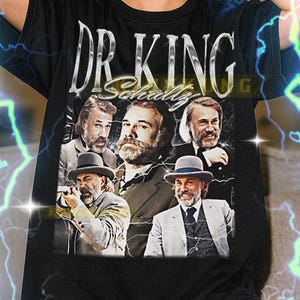 May include: Black t-shirt featuring a graphic of the text "DR. KING" above a collage of images. The images are of a man in various poses. The shirt is a unisex style.