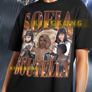 Könnte beinhalten: Schwarzes T-Shirt mit einem Grafikdruck von Sofia Boutellas Gesicht in Collage-Optik mit dem Text "Sofia Boutella" in orangefarbenen Buchstaben mit Glitzer-Effekt.