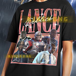 May include: Black t-shirt with a pink graphic print of the text "Lance Reddick" and a group of men. The text "KINGKUNG" is printed in white below the graphic.