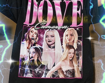 May include: Black t-shirt featuring a pink graphic with the text "DOVE Cameron" and a photo of Dove Cameron. The shirt has a crew neck and short sleeves. The text at the bottom of the shirt is not included.