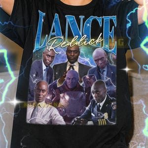 May include: Black unisex t-shirt featuring a collage of images and the name "LANCE Reddick" in blue. The shirt includes images of the actor in various roles. The text at the bottom provides sizing information.