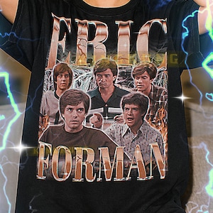 Puede incluir: Camiseta negra con el texto "ERIC FORMAN" y una imagen vintage de un grupo de hombres. La camiseta tiene un diseño retro con un aspecto desgastado. La camiseta es de estilo unisex.