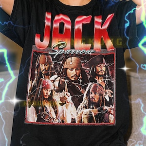 Puede incluir: Camiseta negra con un gráfico de Jack Sparrow de las películas de Piratas del Caribe. La palabra "JACK" está en letras rojas grandes encima de la imagen, con "Sparrow" en cursiva. La camiseta tiene un estilo vintage.