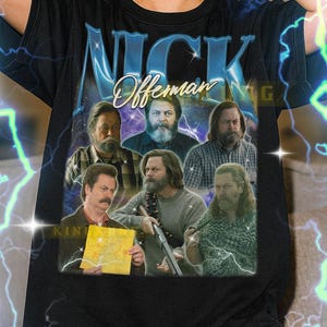 May include: Black t-shirt with a graphic of Nick Offerman and the text "NICK Offerman". The design includes multiple images of the actor. The shirt is a unisex style.
