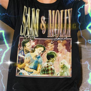 May include: Black t-shirt featuring a vintage-style graphic with the text "SAM & MOLLY" in gold lettering. The graphic includes a framed image of a group of people. The shirt is a unisex style.