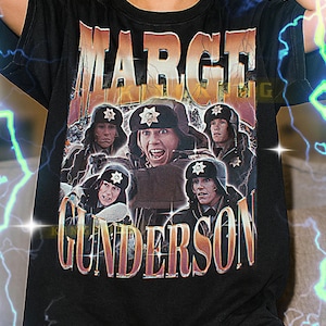 May include: Black t-shirt with a retro graphic design featuring the text "MARGE GUNDERSON" and images of characters in police hats. The shirt has a vintage, distressed appearance.