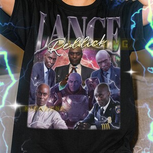 May include: Black t-shirt featuring a graphic of Lance Reddick with the name "LANCE Reddick" in a vintage style. The design includes multiple images of the actor. The shirt is a unisex style.