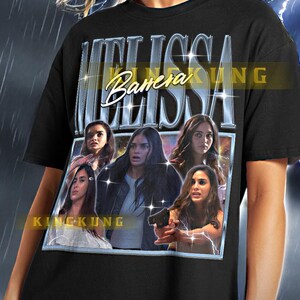 May include: Black unisex t-shirt with a graphic print of Melissa Barrera from the movie "King Kong" with the text "Melissa Barrera King Kong" on the front.