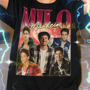Op de afbeelding: Zwart T-shirt met een afbeelding van de band Milo Manheim, met de bandnaam in roze en rood. Het ontwerp heeft een vintage esthetiek. De tekst onderaan het shirt is niet inbegrepen.