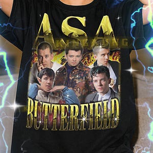 Puede incluir: Camiseta unisex negra con un diseño dorado que presenta un grupo de personas y el texto "ASA" y "BUTTERFIELD". La camiseta tiene un diseño de estilo vintage. El texto en la parte inferior de la imagen dice "El primer modelo lleva una camiseta XL."