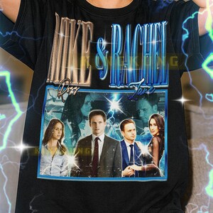 May include: Black t-shirt featuring a graphic with the text "Mike & Rachel" above a framed image of actors. The image has a vintage style with a blue border and lightning bolt accents. The shirt is unisex.