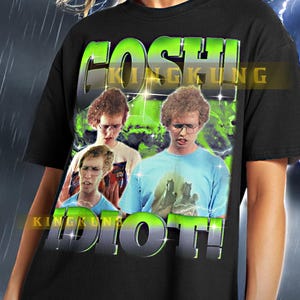 May include: Black graphic t-shirt featuring the text "GOSHI IDIOT!" in green and white. The shirt displays a collage of images of a person wearing glasses. The shirt is a unisex style.