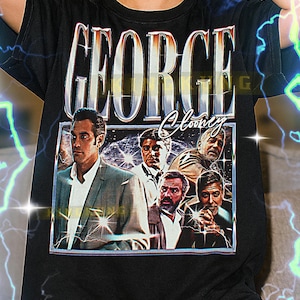 May include: Black t-shirt featuring a graphic of George Clooney and the text "GEORGE Clooney" in a vintage style. The shirt has a crew neck and short sleeves. The image on the shirt shows a group of men in suits.