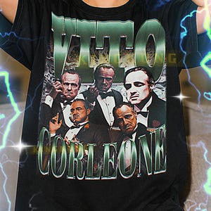 May include: Black t-shirt featuring a graphic of several men in suits with the text "VITO CORLEONE" in green. The shirt is a unisex design and is available in various sizes.